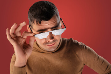 Man wearing pixelated sunglasses looks at the camera,  wearing a brown sweater  adjusting his...