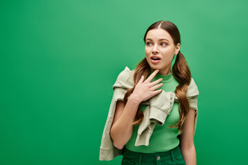 A young woman in her 20s in a green shirt holds her hands peacefully on her chest in a studio setting.