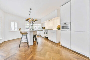 Bar chairs at table with decoration placed in spacious stylish kitchen with white cupboards and...