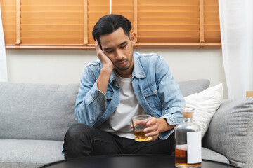 melancholy young Asian man drinks alcoholic whisky alone at home feeling dizzy after drunk