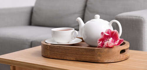 Teapot and cup of hot tea with tulip flower on table in living room