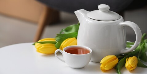 Cup of hot tea, tulips and teapot on table in room