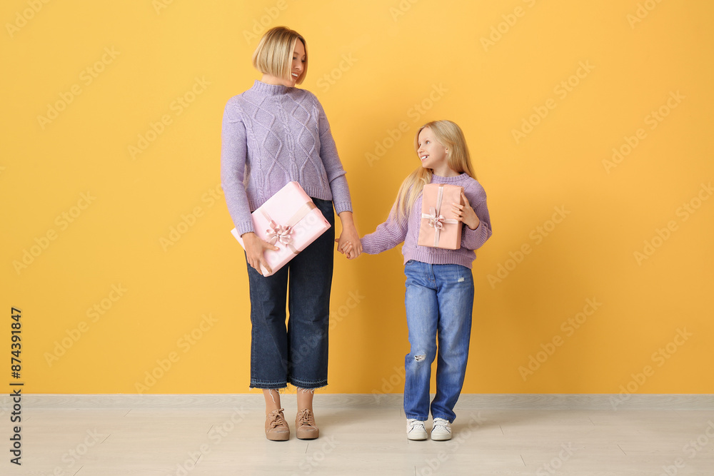 Poster beautiful young woman with her cute little daughter holding gift boxes near yellow wall