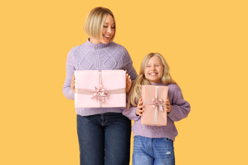 Beautiful young woman with her cute little daughter holding gift boxes on yellow background