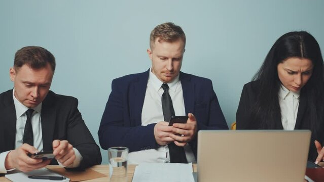Business team members use their break to engage with their smartphones, highlighting mobile dependency and digital addiction in workplace