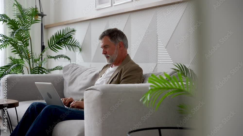 Poster confident mature man typing on laptop while sitting on sofa in living room at home office. freelance