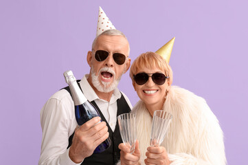 Mature couple in party hats with champagne on lilac background