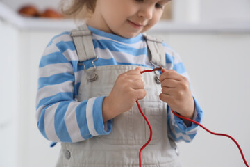 Cute little girl with bare wire in kitchen, closeup. Child at risk
