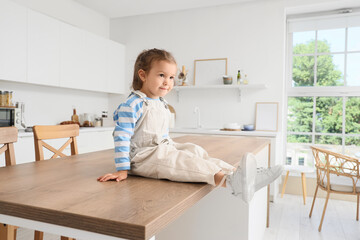 Cute little girl sitting on high table in kitchen. Child at risk