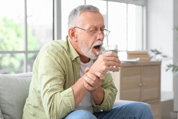 Senior man suffering from Parkinson syndrome drinking water at home