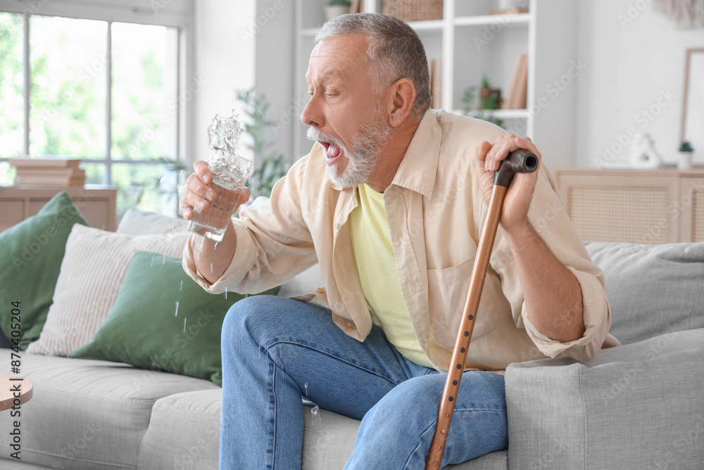 Sticker senior man suffering from parkinson syndrome with stick drinking water on sofa at home