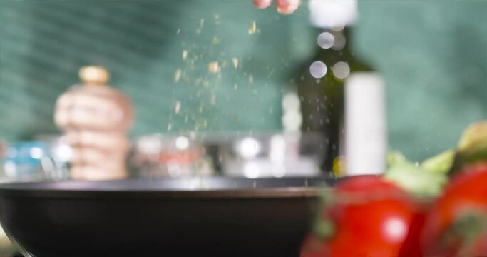 The chef's hand sprinkles herbs liberally over the dish.
