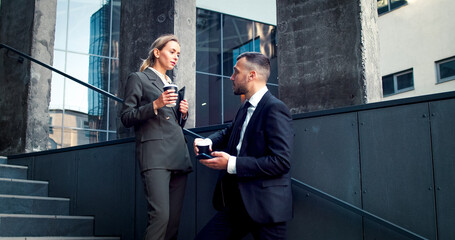 Portrait of two managers standing on stairs of buiding of business center. Businesspeople have small talk within coffee break between work.