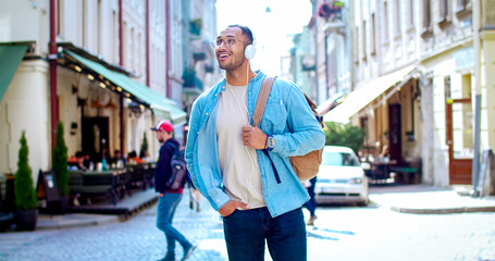 Portrait of American tourist wearing glasses walks down street in the morning. Handsome excited man...