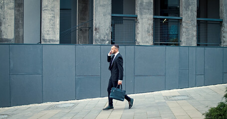 Businessman with bag in hand goes to work speaking on phone. Caucasian male wearing business suit...