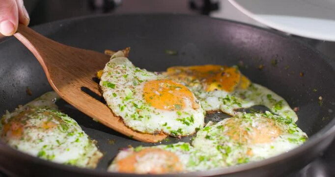 The cook takes an egg out of the pan with a wooden spatula.