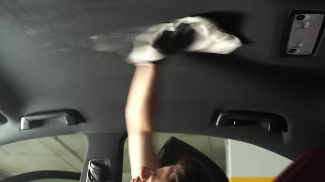 4k video detailing car headliner covering. Spraying detergent on the headliner in car. Hand cleans car ceiling with detergent and microfiber rug.