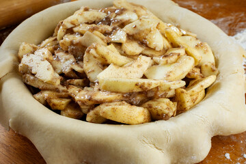Making a pie.   Rolled dough placed over a pie shell and filled with sliced apple filling.  Top side view.