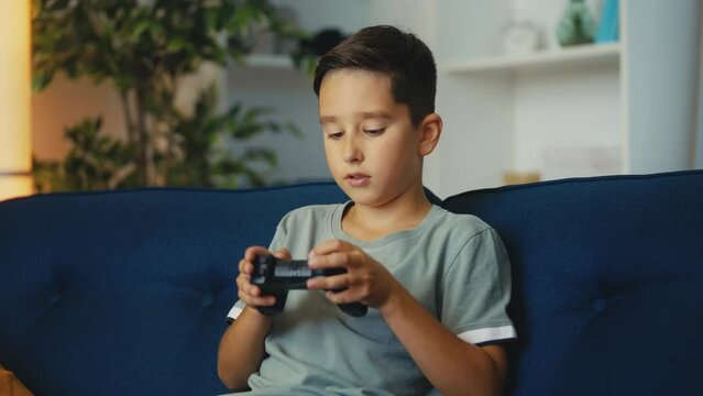 Focused young boy playing video game at home using gamepad, gaming hobby