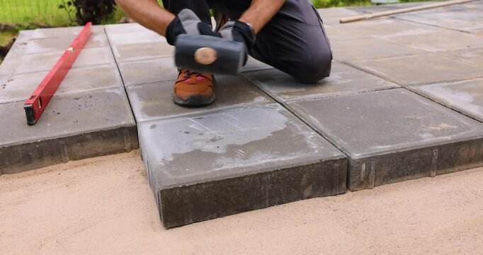 worker installing concrete paving slabs on sand foundation. driveway pavement