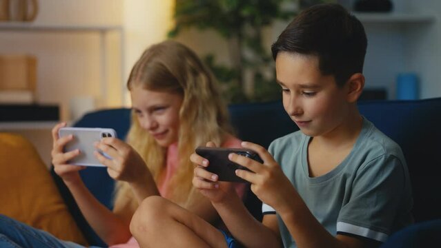 Smiling pre-teen girl and boy playing online multiplayer game on their phones