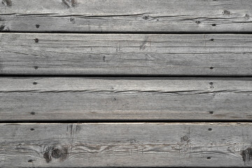 Texture of a gray house wall made of old cracked wooden planks fixed with screws as a background