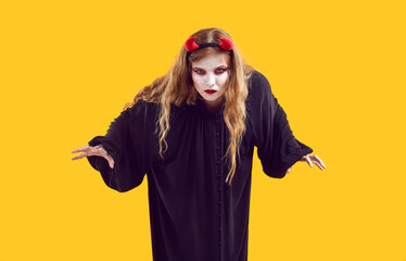 Young girl wearing evil devil disguise isolated on yellow background. Woman dressed in Halloween...