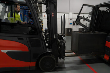 Forklift truck driver pulling a battery out of another forklift truck to load it