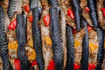 limbazi, Latvia, June 29, 2024 - Close-up of grilled fish stuffed with red and yellow bell peppers, arranged in rows. The fish appear charred and well-cooked.