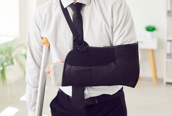 Office worker in formal wear with trauma, broken arm, leg, man wearing arm support with walking...