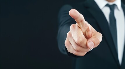 Close-up of a hand in a suit pointing forward on a dark background, symbolizing direction, focus, or decision.