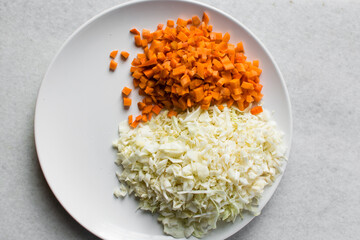 Overhead view of diced carrots and shredded cabbage on a white plate, top view of sliced carrots and cabbage on a marble countertop