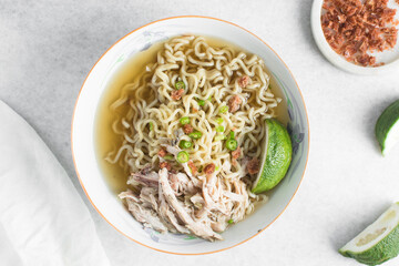 Overhead view of noodles in clear broth with shredded chicken and a lime wedge, top view of ramen noodles in chicken broth on a marble countertop