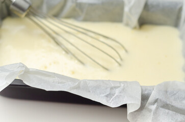 A whisk is sitting in the dough in a loaf tin with a sheet of parchment paper