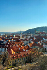 Obraz premium Panoramic view of the city of prague with its red roofs, churches and bridges under a blue sky in Prague