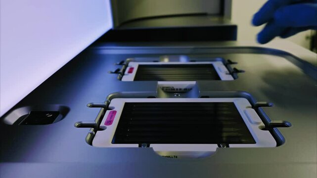 DNA sequencer. Gloved hand is handling flow cell with multiple lanes for DNA samples placed inside sequencer, prepared for sequencing. High-tech laboratory environment, genetic analysis and research