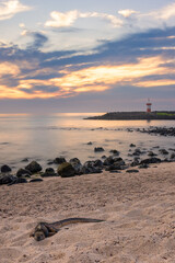 Atardecer y larga exposición en bahía de costa con iguana marina en prime plano y faro en el...