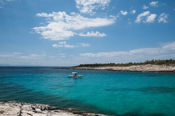 A small boat on the turquoise blue water along the rocky shore of Atspas beach on the island of Thassos in Greece