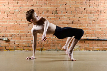 Young male dancer performing a modern dance routine in an urban setting, shirtless in front of a brick wall