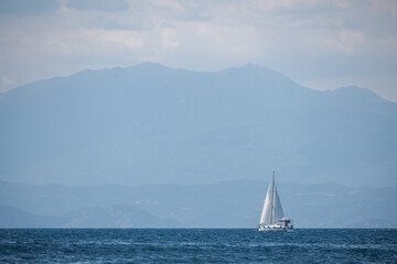 A white sailing boat on the horizon sails on a calm sea