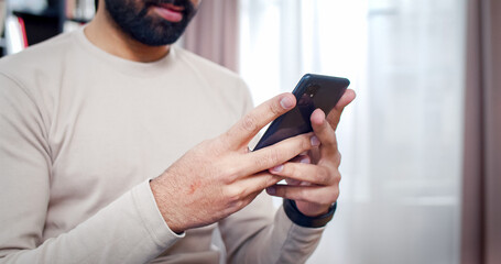 Close up portrait of hands with phone in. Bearded face man putting fingers on gadget screen types new massage to friend.