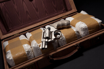 A revolver lies on top of bundles of
powdered drugs in a briefcase Studio
shot