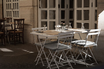 Outdoor empty coffee and restaurant terrace with white tables, vintage chairs and wine glasses in Europe. Cafe terrace on the pedestrian street in Rome, Italy. A set table is waiting for customers.
