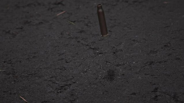 Single empty bullet shell casing falling and bouncing on asphalt ground in 1000fps slow motion	