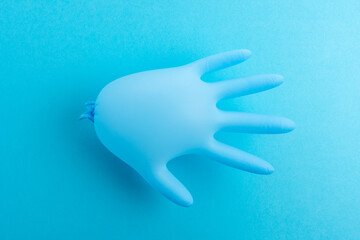 Blue latex medical glove on pastel blue backdrop. Minimal Coronavirus outbreak. Panic concept.