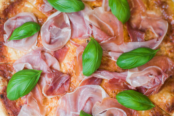 Delicious pizza slices with prosciutto, cheese and basil. Close-up of a pizza in the American style.