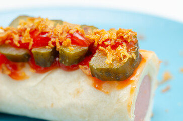 A hot dog wrapped in a tortilla with pickles and ketchup on top