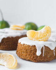 Iced mini bundt cake on a white tray, vanilla bundlette cakeswith a clementine segment on a white background, small vanilla bundt cakes with an icing glaze