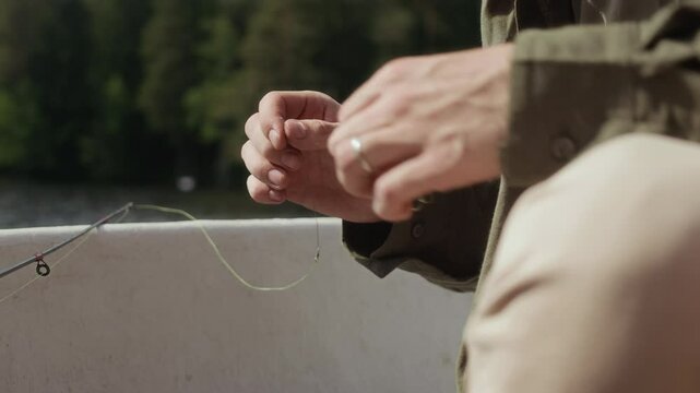 Cropped shot of unrecognizable fisherman putting bait on fishing hook while sitting in fishing boat on sunny day