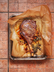 A piece of cooked meat on the bone is sitting on a cooking paper and tray with a few herbs on top....